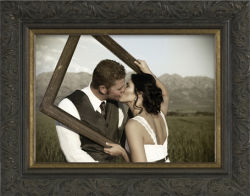 Custom frame design with young couple kissing through an empty frame with mountains and fields in the background.
